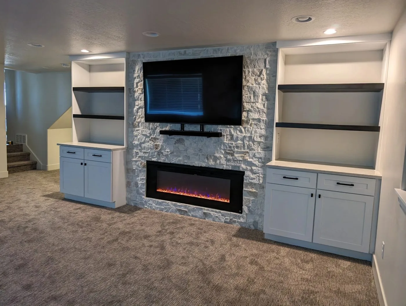 Finished basement with stone fireplace wall, floating shelves, and built-in cabinets