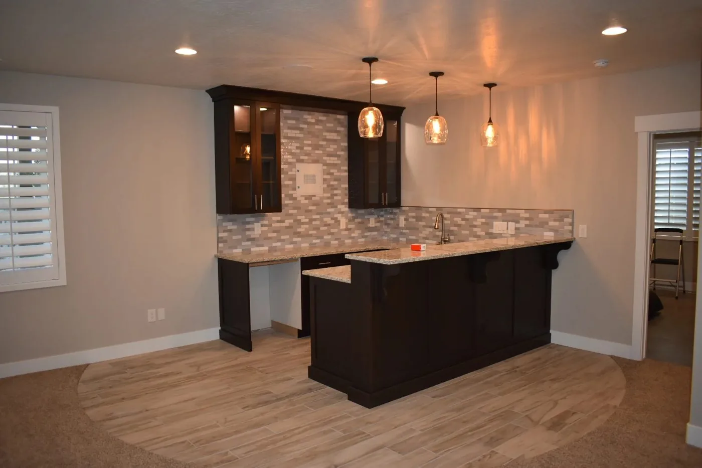 Dark custom cabinetry with stone backsplash and pendant lighting